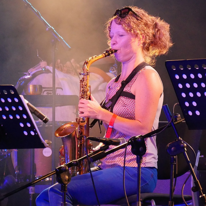 A photo of Kasey Knudsen playing the saxophone while live on stage. A photo of Kasey Knudsen playing the saxophone while live on stage.