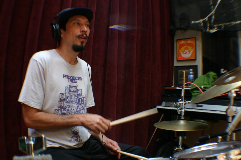 A photo of Josh Jones sitting at his drum set, playing the drums in the Wide Hive Studio.