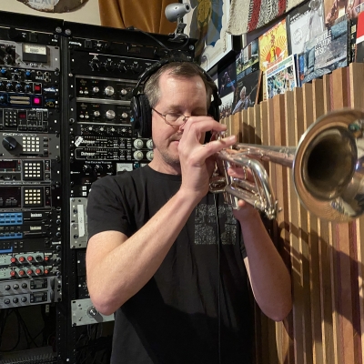 Erik Jekabson playing a trumpet in front of a rack at Wide Hive Records. A photo of Erik Jekabson playing a trumpet in front of a rack at Wide Hive Records.