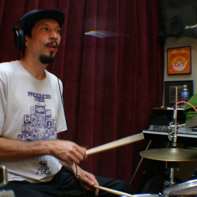 A photo of Josh Jones sitting at his drum set, playing the drums in the Wide Hive Studio.