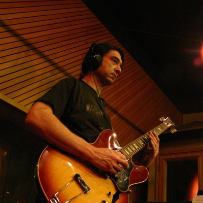 A photo of Mike Ramos playing guitar in the Wide Hive Studios.